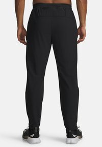 Zwarte sportieve broek met een elastische tailleband en een rits achterzak. Tapered ontwerp, gemaakt van lichtgewicht materiaal, gecombineerd met stijlvolle sneakers.