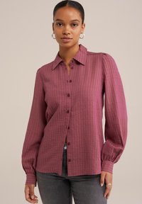Camicia button-up in tessuto bordeaux testurizzato, con colletto, maniche lunghe a sbuffo e un sottile motivo a griglia. Chiusura frontale con bottoni.
