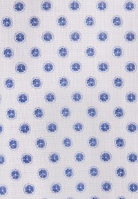 Tissu blanc avec une texture en grille structurée de petits cercles bleus uniformément espacés, chacun contenant un motif floral bleu plus foncé.