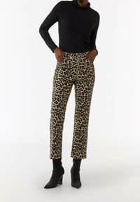 Luipaardmotief broek in beige en zwart, met voorzakken en een rechte snit, gecombineerd met een zwart shirt met lange mouwen en zwarte hoge laarzen.