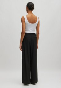 Weißes Tanktop mit tieferem Rückenausschnitt, kombiniert mit hoch taillierten, schwarzen, weiten Hosen. Geschmeidige Textur, minimalistisches Design, keine sichtbaren Muster.