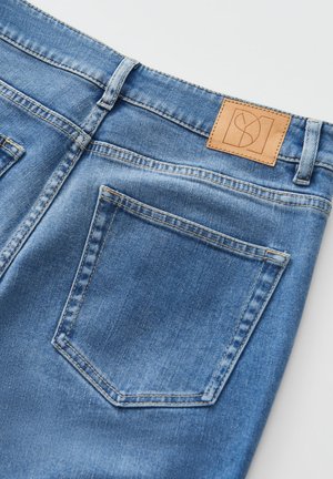 Blue denim jeans featuring a tan leather patch at the back waistband, two back pockets, and a smooth, textured finish.