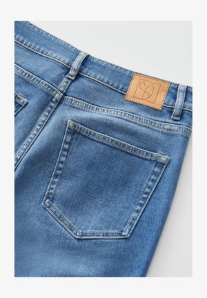 Blaue Jeans aus Denim mit einem hellbraunen Lederpatch am hinteren Bund, zwei Gesäßtaschen und einer glatten, strukturierten Oberfläche.