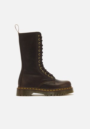 Stivale alto in pelle marrone scuro con lacci, cuciture gialle, suola spessa rigata e anello di tiraggio sul retro.