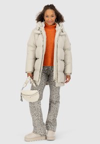 Doudoune gris clair, pull en tricot orange, pantalon à motifs gris et noir façon animal, sac crème et chaussures à plateforme beiges.