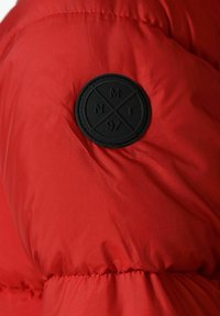 Tissu de doudoune rouge avec une texture lisse. Présente un patch en caoutchouc noir de forme circulaire avec des lettres en relief et des lignes croisées.