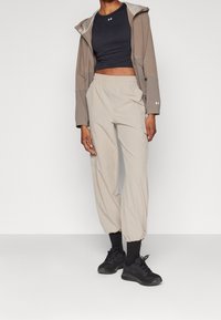 Pantaloni jogger leggeri di colore beige con vita elastica e polsini affusolati, abbinati a un top corto scuro e a una giacca con cappuccio marrone.