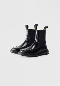 Botine negre din piele cu panouri laterale elastice, mânere de tragere și talpă din cauciuc rezistent. Prezintă o textură netedă și cusături decorative.