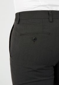 Anthrazitgraue Hose aus strukturiertem Gewebe, mit einer Gesäßtasche mit einem schwarzen Knopf und Gürtelschlaufen an der Taille.