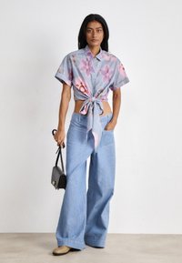 Camicia azzurro chiaro a maniche corte legata in vita, abbinata a pantaloni in denim azzurro chiaro a gamba larga e una piccola borsa nera.