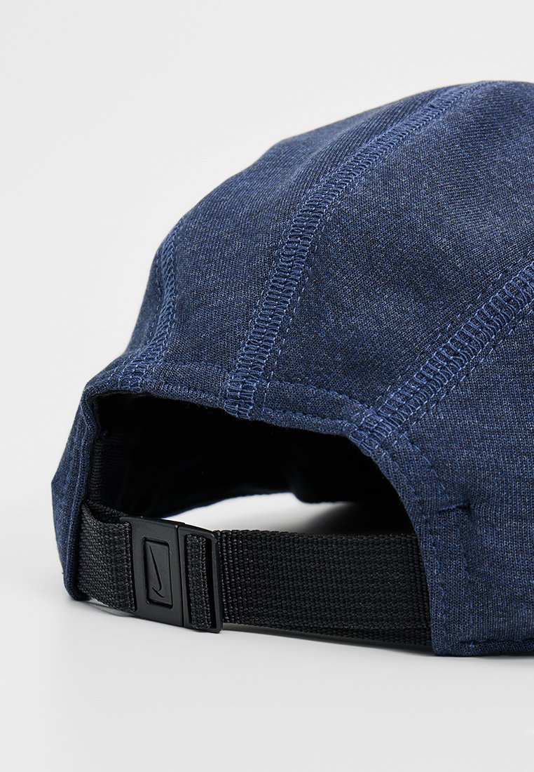 Vista trasera de una gorra de tela azul marino con costuras visibles y una tira ajustable negra con un cierre con el logo de Nike.