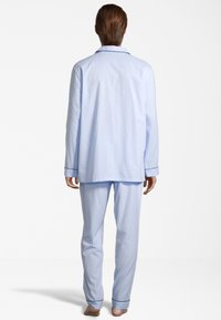 Vaaleansininen puuvillapaitapuku, johon kuuluu napitettavalla yläosalla, jossa on pitkät hihat, ja housut, joissa on kontrastoiva tumma resori.