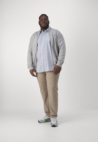 Cárdigan gris sobre una camisa blanca con flores, pantalones beige y zapatillas en gris, verde y negro. Ajuste casual con un diseño relajado.