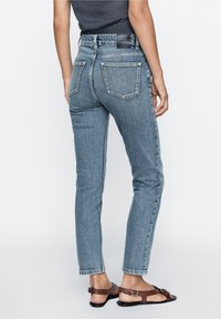 Jeans taille haute bleu clair avec une silhouette ajustée, cinq poches et un design minimaliste. Le tissu a une légère texture.