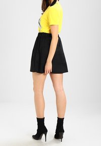 Gul t-shirt med korta ärmar och logotypdesign, ihopparad med en svart, lager på lager kjol, ankellånga strumpor och högklackade skor.