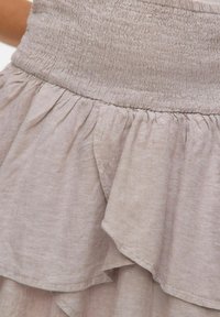 Lys beige volangskjørt med smocket midjebånd, myk lintekstur og lagdelt stoffdetalj langs kanten.