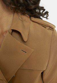 Camel trenchcoat met een scherpe kraag, één borstzak en een gladde, gestructureerde stof voor een stijlvolle uitstraling.
