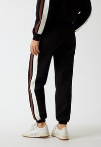 Zwarte joggers met witte en bruine zijstrepen, met cuffed ankels en een elastische tailleband; gecombineerd met witte sneakers.