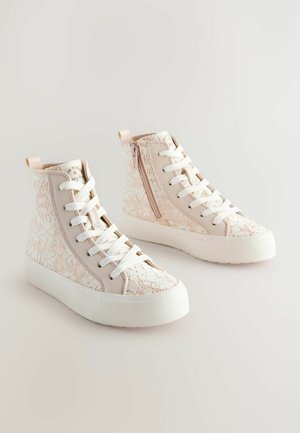 Wysokie sneakersy z fakturowanym wzorem sznurków w jasnoróżowym kolorze, z białymi sznurówkami i bocznym zamkiem błyskawicznym, spoczywające na białej gumowej podeszwie.