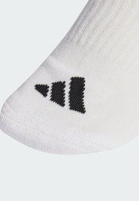 Biała sportowa skarpeta o fakturowanym wykończeniu z czarnym logo na okolicy kostki. Materiał wydaje się lekki i elastyczny.