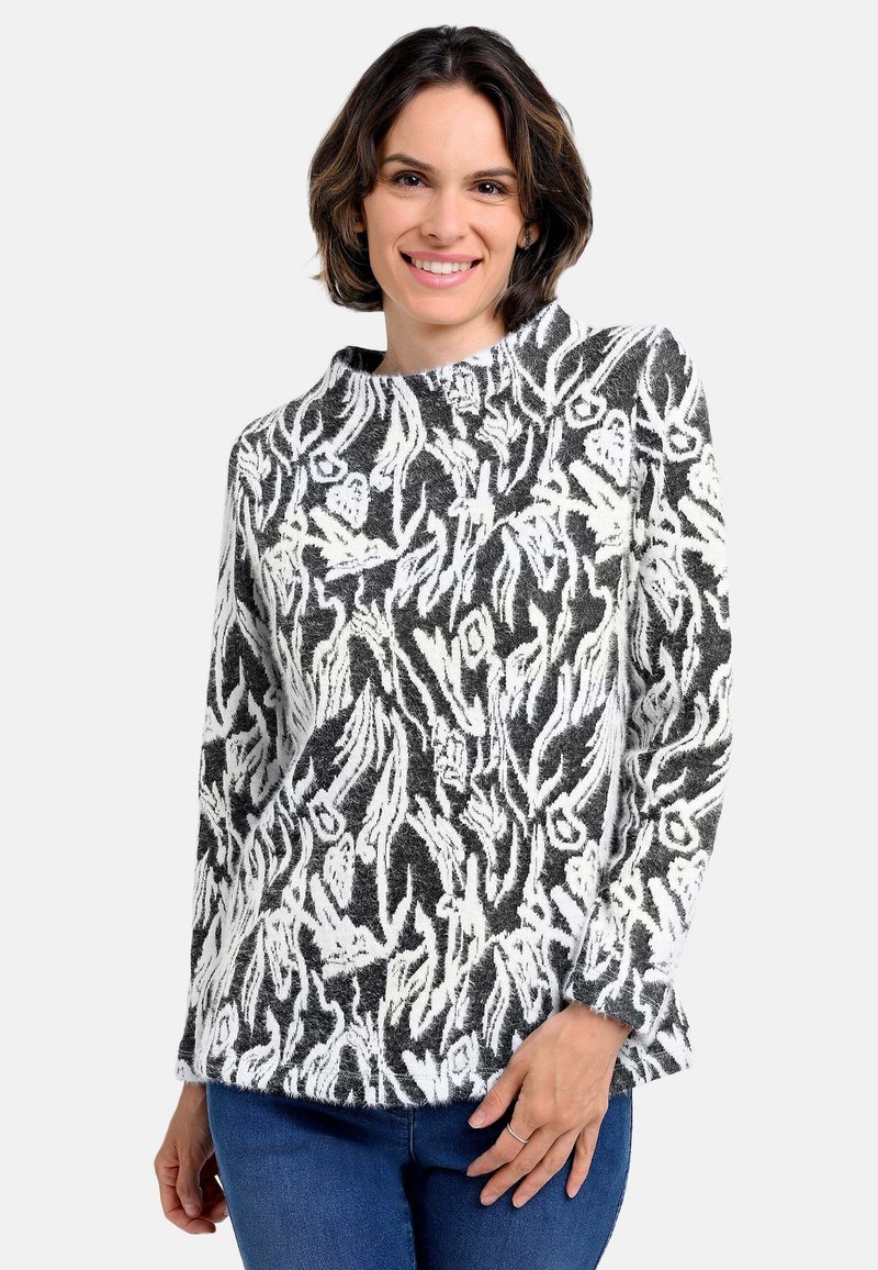 Langärmeliges Strickoberteil mit schwarz-weißem Blumenmuster, weicher Textur und hohem Kragen, kombiniert mit blauen Jeans.