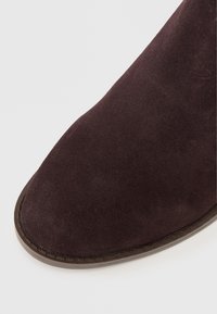 Tamno ljubičasta suknja s rondastim vrhom i strukturiranom površinom. Potplat ima kontrastni smeđi obrub i malo je podignut.