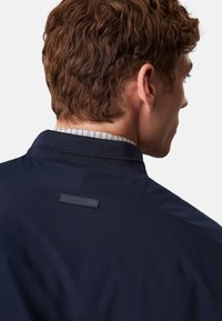 Giacca blu navy con colletto strutturato, caratterizzata da un tessuto testurizzato e una piccola etichetta Calvin Klein sul retro.