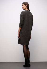 Sukienka dzianinowa w ciemnobrązowym kolorze z subtelnym wzorem, długimi rękawami i zaokrąglonym dekoltem, zestawiona z czarnymi botkami do kostki. Gładka tekstura.