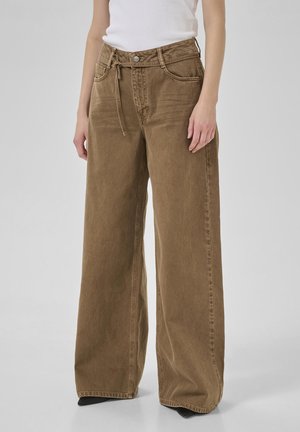 Weite, braune Cord-Hosen mit hoher Taille, verstellbarem Bindegürtel, Fronttaschen und sichtbaren Steppdetails.