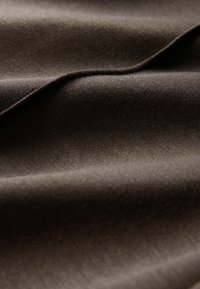 Donkerbruin stof met een gladde textuur, met zachte plooien en een subtiele glans. Het materiaal lijkt zacht en dicht geweven.