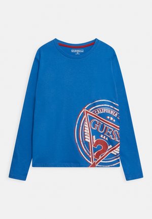 Blå langærmet skjorte med rødt og hvidt Guess-logo og teksten California trykt i nederste højre side.