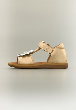 Beige toddler sandal with Velcro strap and white flower decoration on front, brown sole, and closed heel.