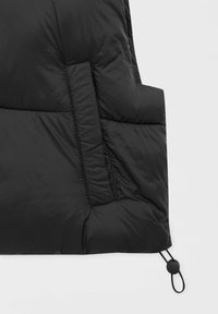 Černá prošívaná tkanina s vertikální obdélníkovou kapsou a nastavitelnou šňůrkou s brzdičkou v pravém dolním rohu.