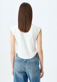 Witte mouwloze top met een ronde zoom, gecombineerd met lichtblauwe high-waisted spijkerbroek. Gladde textuur met minimale stikdetails.
