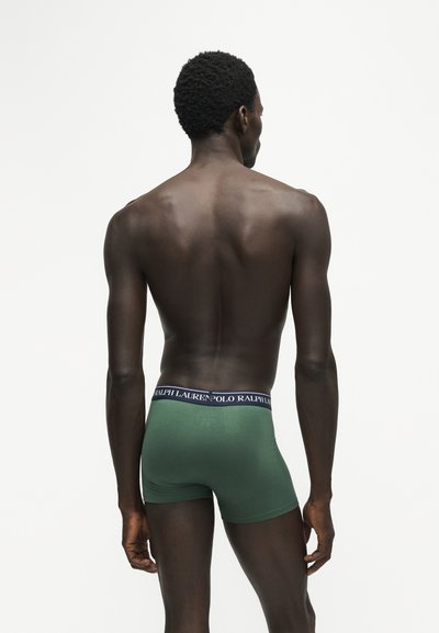 Πίσω όψη λεπτού άνδρα που φοράει πράσινα boxer briefs Ralph Lauren, στέκεται μπροστά σε απλό λευκό φόντο.