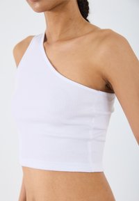 White ribbed crop top featuring an asymmetrical one-shoulder design. Soft texture with a fitted shape and clean, simple hems.