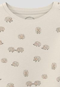Helles beige Shirt mit rundem Ausschnitt, das ein sich wiederholendes Muster von Igeln in Braun- und Pastellfarben zeigt. Weicher Baumwolltextil.