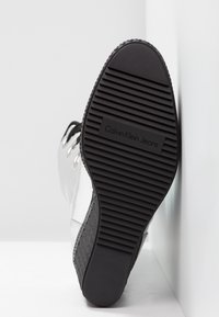 Semelle extérieure d'une chaussure à semelle noire avec des rainures horizontales et le logo "Calvin Klein Jeans" embossé au centre.