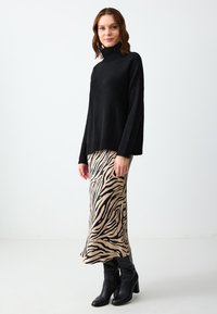 Maglione nero lavorato a maglia con collo alto, abbinato a una gonna beige con stampa zebra nera. La modella indossa stivali neri con tacco al ginocchio.