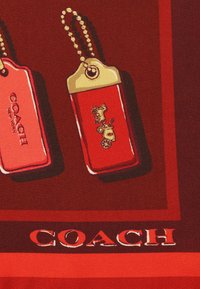 Rød silke tørklæde med to røde mærke designs med guld accenter, hvoraf det ene viser en hest og vogn, samt "COACH" branding i fed skrift.