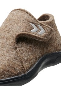 Brun filttoffla med en texturerad yta, som har en svart gummisula och en kardborreband som accentueras av två vita chevroner.