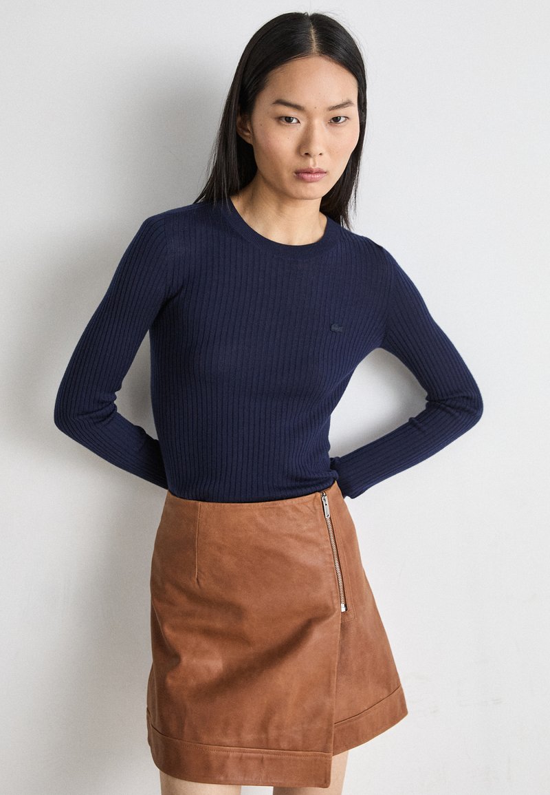 Marineblauw ribbeltrui met lange mouwen, gecombineerd met een bruine leren minirok met een zijrits, die gladde texturen en aansluitende silhouetten benadrukt.