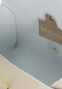 Interiér béžové kabelky, s hladkou texturou a světlomodrou látkovou podšívkou. Obsahuje béžovou etiketu s embosovaným nápisem "wojas".