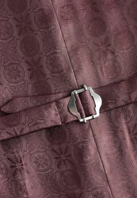 Tissu bourgogne avec un motif en relief complexe comportant des motifs circulaires et des accents floraux, fixé avec une boucle en métal.