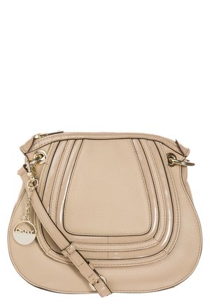 Sac bandoulière en cuir beige avec des accents de design courbés, des métaux dorés, une fermeture zippée et un pendentif rond doré avec le logo DKNY sur la sangle.