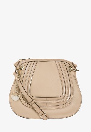 Sac bandoulière en cuir beige avec des accents de design courbés, des métaux dorés, une fermeture zippée et un pendentif rond doré avec le logo DKNY sur la sangle.