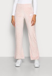 Rosa velour sweatpants med vitt Nike-logotyp och upprepande varumärkesmönster. Utsvängda ben, mjuk textur och elastisk midja.