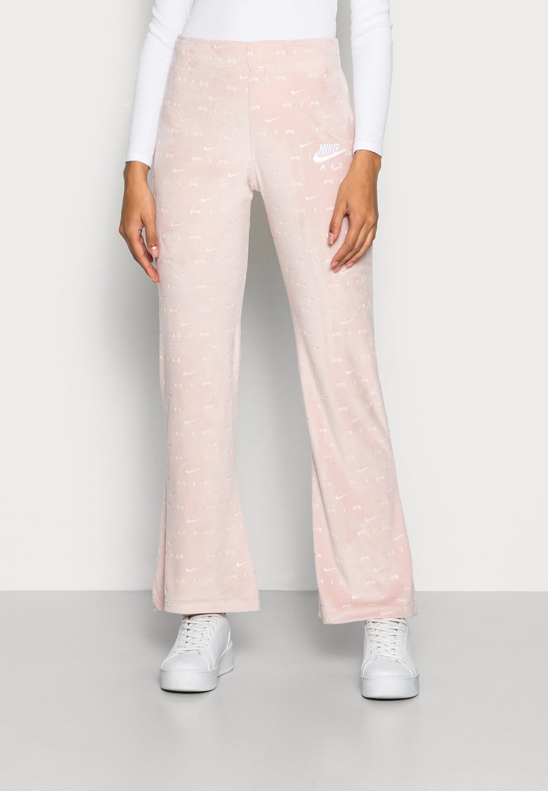 Rosa velour sweatpants med vitt Nike-logotyp och upprepande varumärkesmönster. Utsvängda ben, mjuk textur och elastisk midja.