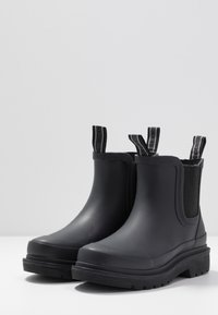 Bottes de cheville en caoutchouc noir avec des panneaux latéraux élastiques, des semelles texturées et des languettes pour un enfilage facile. Surface lisse et sans motifs visibles.