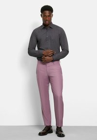 Camicia a maniche lunghe con motivo scuro, colletto abbottonato, abbinata a pantaloni rosa chiaro e scarpe stringate marroni.